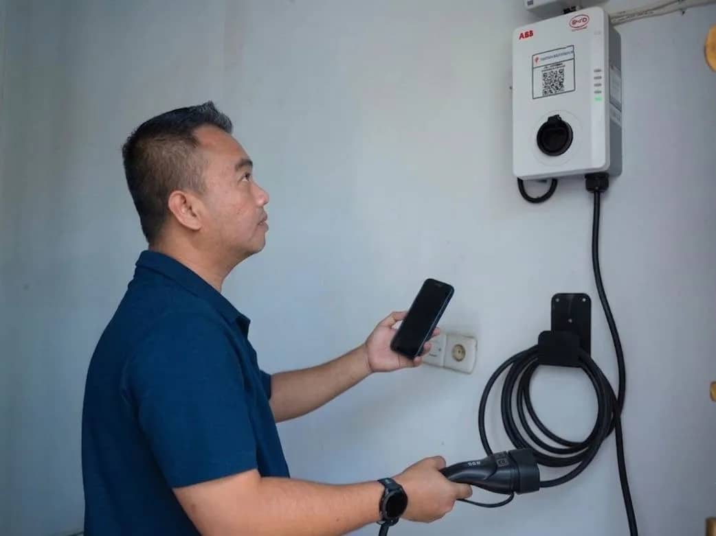 Seorang pelanggan PLN di Papua menggunakan handphonenya untuk mengatur pengisian daya kendaraan listrik melalui perangkat Home Charging di rumahnya.